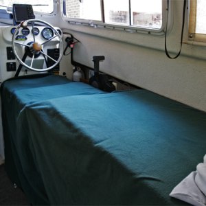 Starboard side made up into 6 ft + bed by lowering galley covers, adding extender cushion and support, then removing seatback and moving to front of bottom. Seat back is held by strap around steering wheel snapped into the existing snaps on the seatback. A support slides out from under seat bottom to support the seatback; very simple to deploy.