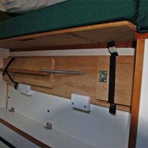 Bed support for the starboard bed is stowed on the  port-side box. Note the extender support  holding the port extender cushion. It can be quickly slid back under the lid to allow use of the original cushion for the 2 position commuter seat. The starboard bed support rests on a wood block at each end and is captured by the slotted fingers; it is rock solid with the leg extended. The storage box with lid is 40 inches long and holds kitchen items.