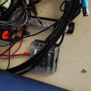 Sea Angel\'s Secondary AUX 6 ckt DC power block & 10x ground buss 2a. The rectanguliar 'bar' above the square Secondary AUX DC power panel is a 10X #8-32 negative ground buss bar. It has a plastic removeable protective push on cover. It is strapped to the main 12 ckt MAIN AUX Negative ground stud post with a copper link. 
The black "cables" laying above the power blocks are the steering's hydraulic lines.