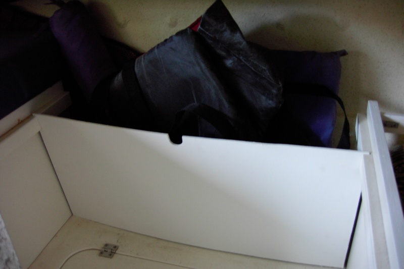 Simple shelf. Cut two slits in the starboard at an angle.This allows the board to lean out at the top for more room and still allow the hatch below to open. Notch out 1/8" ply for the table leg when dropped to bed configuration. Then slide in wood. This holds a bunch of bulky stuff such as PFD's, boat cushions,frisbee's, dogs water toys and a beach shade tent.  Two swim noodles lay fore and aft across the top. Ventalation is such that damp items can still air out. Want to reconfigure to a stock boat?  Just lift out the board.The factory carpet still fits underneath.